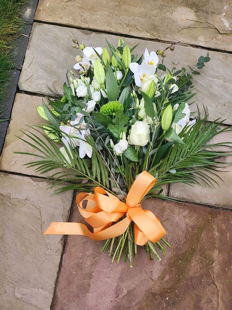 Presentation sheaf of white lilies, roses and orchids with a peach ribbon on stone paving