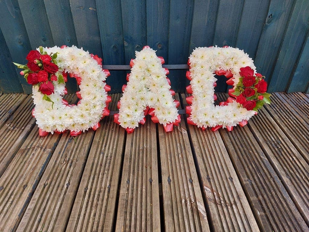 Letter tribute spelling DAD in white chrysanthemums with red ribbon trim and red rose clusters