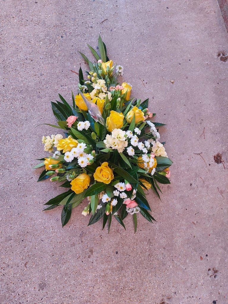 Teardrop funeral spray of yellow roses, white daisies and cream stocks on dark foliage