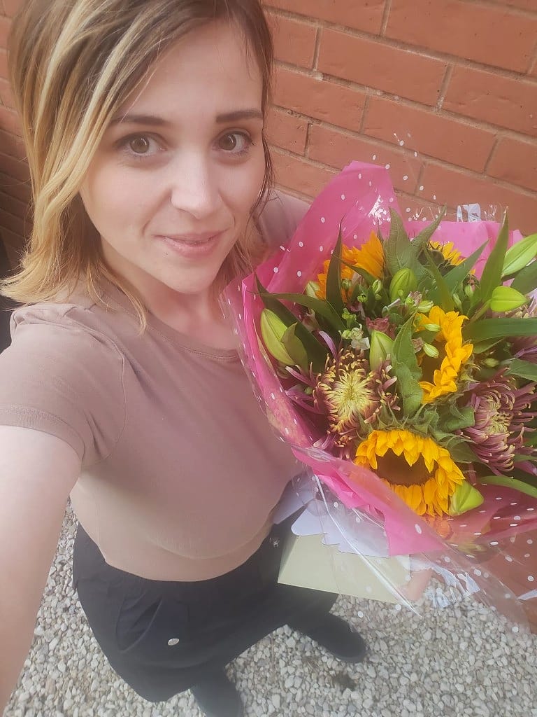 Megan holding a sunflower and chrysanthemum bouquet wrapped in pink spotted cellophane