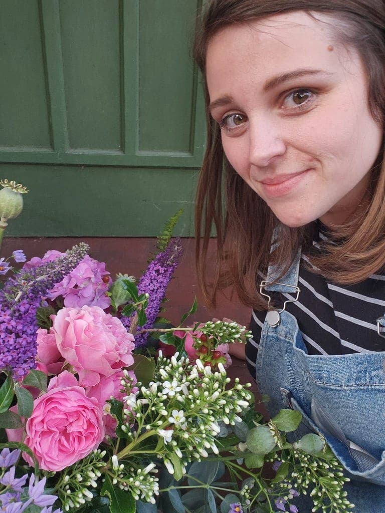 The Floral Vibe florist with pink roses and purple buddleia, wearing dungarees
