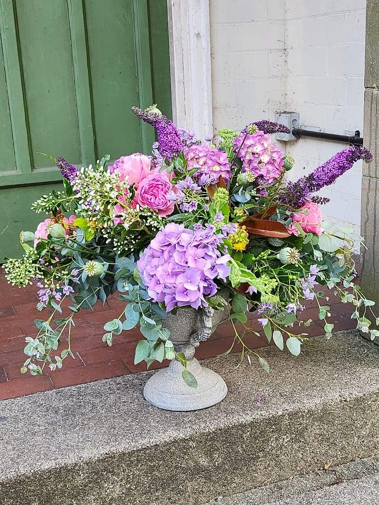 Garden-style arrangement of purple hydrangeas, pink roses and buddleia in a stone urn