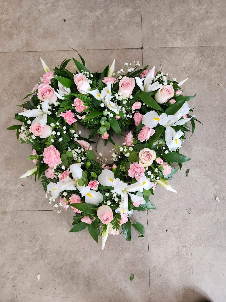 Heart-shaped tribute of pale roses, irises and gypsophila, made with softness and care
